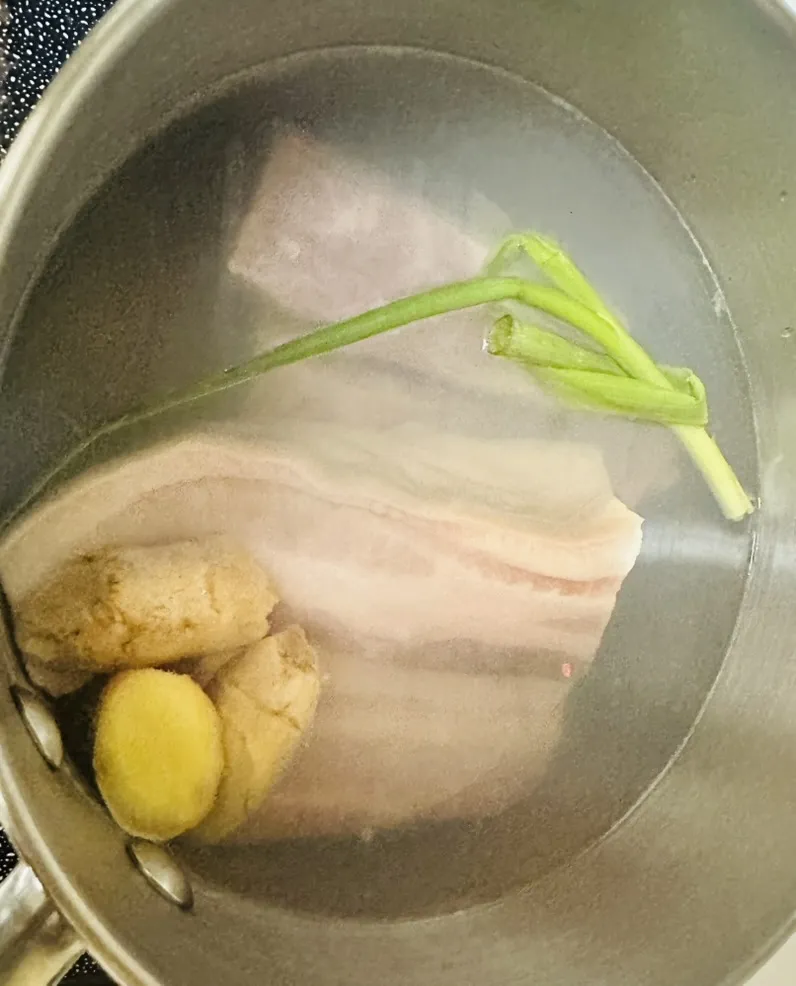 Pork belly blanching in a pot of water with ginger and Shaoxing wine