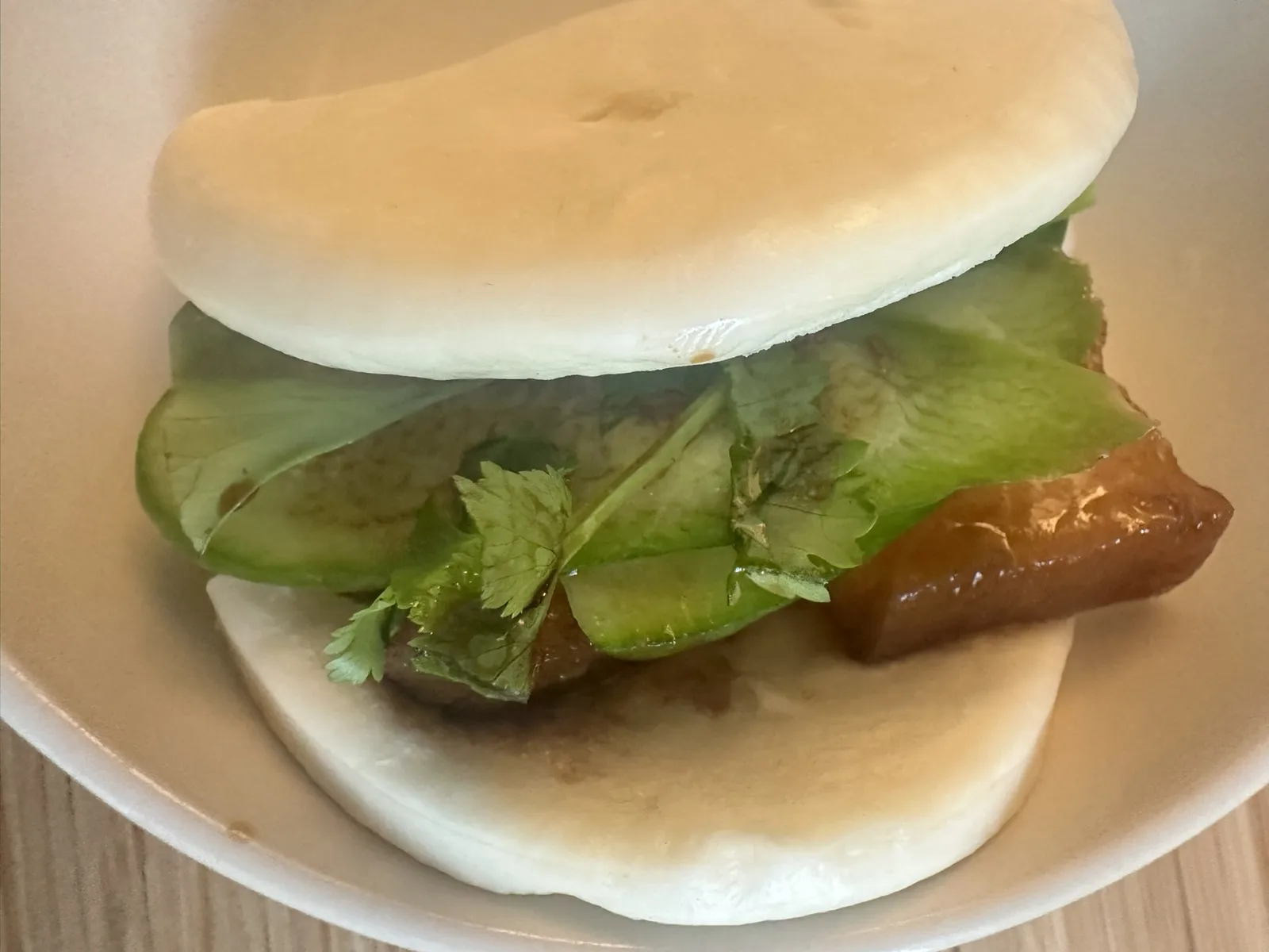 Assembled steam bun with red-braised pork belly, cucumber, and cilantro