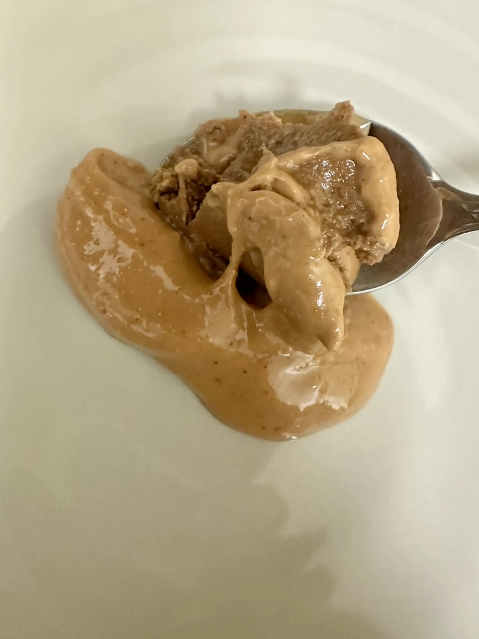 A thick scoop of peanut butter and Chinese sesame paste sitting undiluted in a white bowl with a spoon.