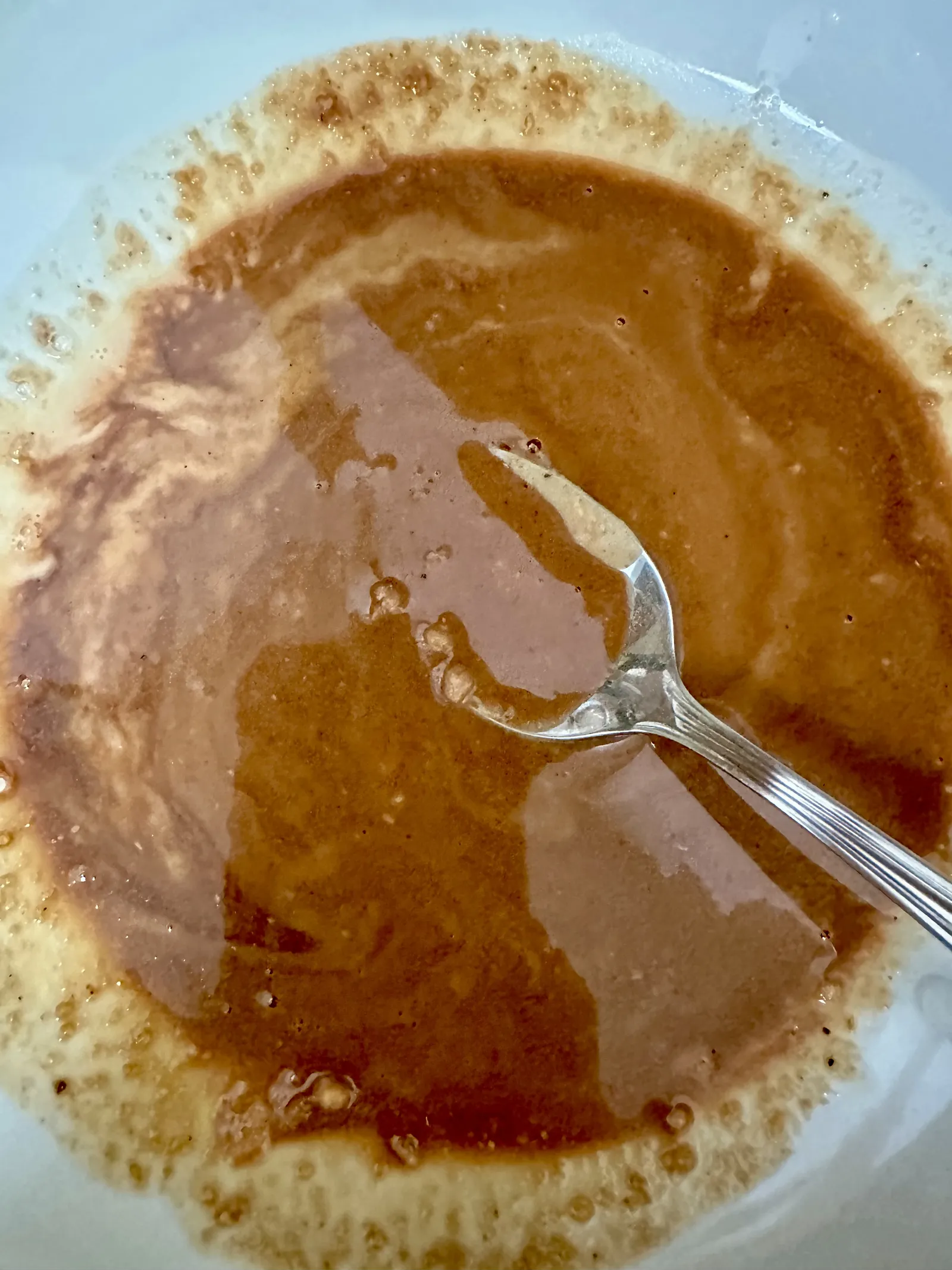 The same paste thinned with hot noodle water into a glossy, pourable sauce, being stirred with a fork.